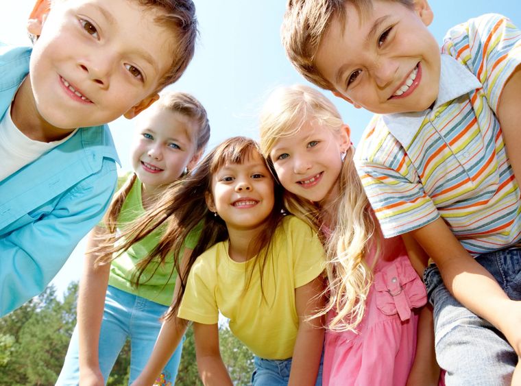 Five smiling children leaning together in a circle outdoors