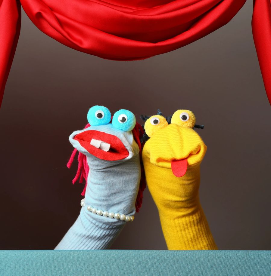 Two colourful sock puppets performing behind a red stage curtain