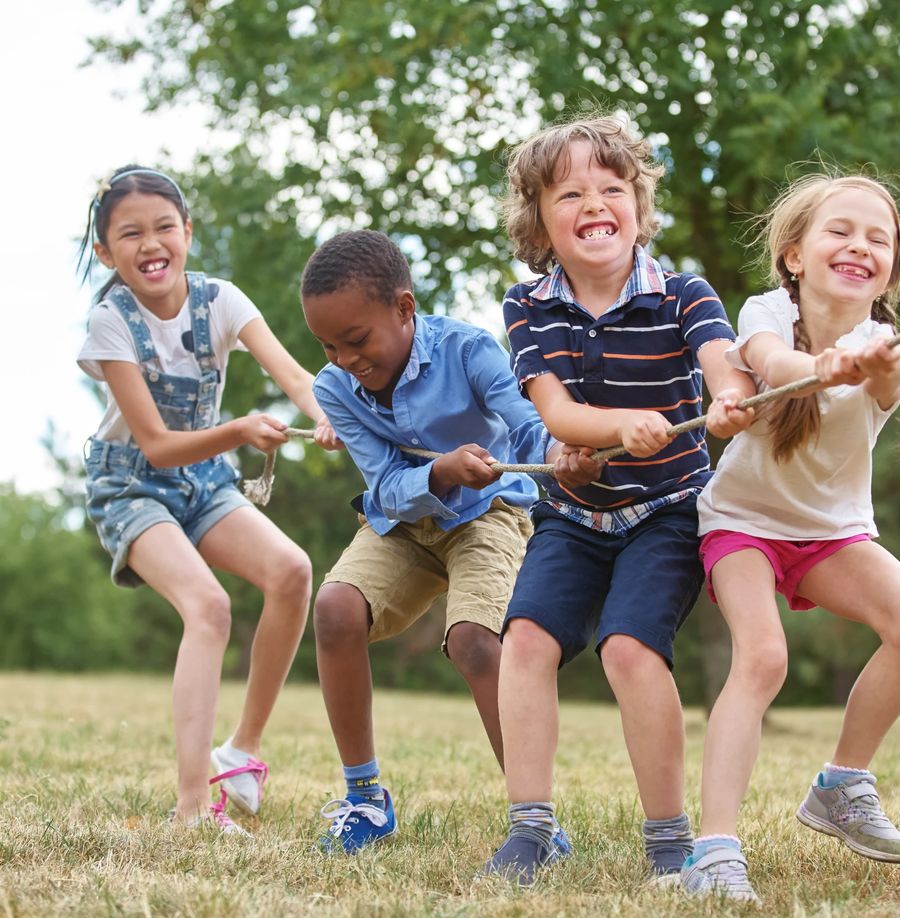 Four children laughing as they pull a rope in a tug of war on grass
